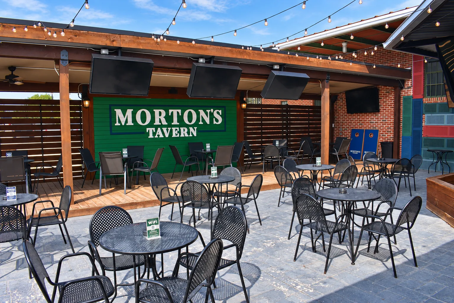 Pet-friendly patio with tables, string lights, and TVs at Morton's Tavern in Fort Worth